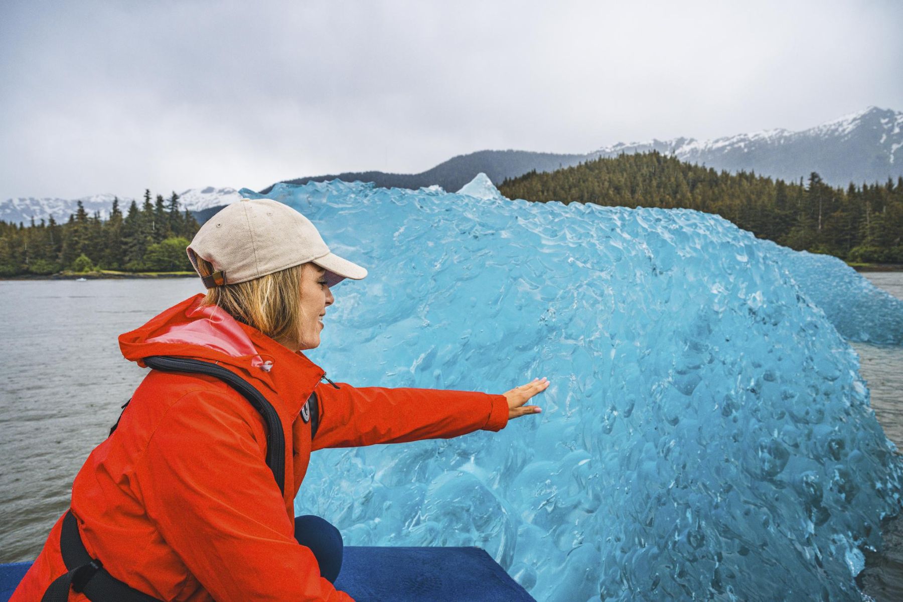 Woman touching an iceberg on a Stikine River Jet Boat Tour