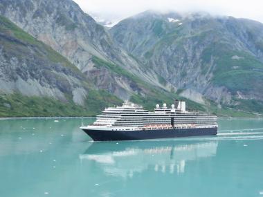 A cruise ship glides through an Alaska bay with mountains in the background