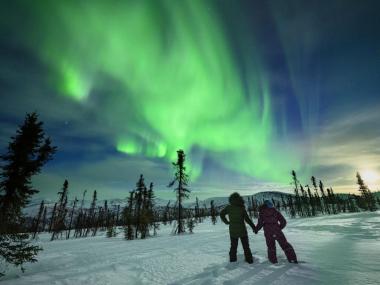 Two people hold hands and watch the northern lights in Fairbanks.