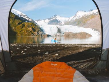 Person in tent looking out at person packrafting
