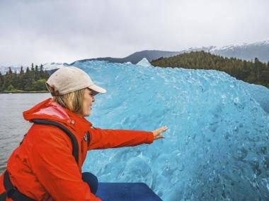 Woman touching an iceberg on a Stikine River Jet Boat Tour