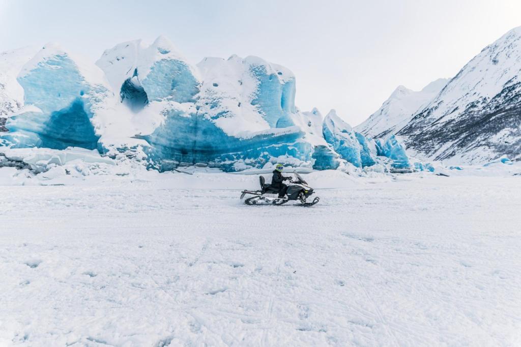 A person on a snowmachine in front of a glacier on a snowmachine tour
