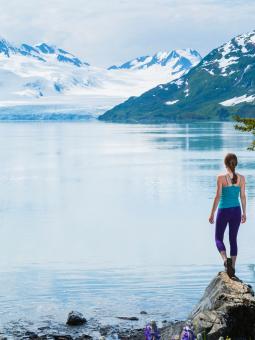 A woman looks out onto a lake surrounded by snowy peaks
