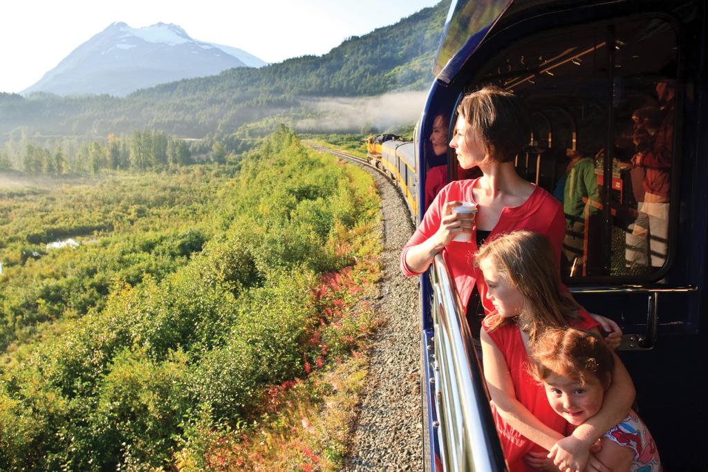 A woman and her two daughters standing on the GoldStar Viewing Platform look out onto the landscape as they ride Alaska Railroad's Coastal Classic Train